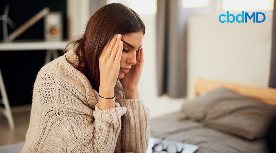A woman sitting on her bed with her hands on her head stressed out