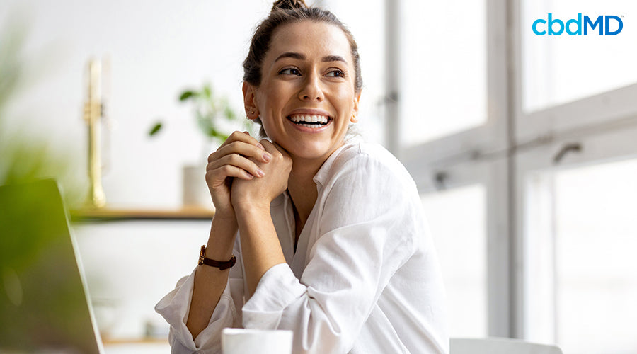 A woman smiling that is sitting down at a desk with a laptop on it