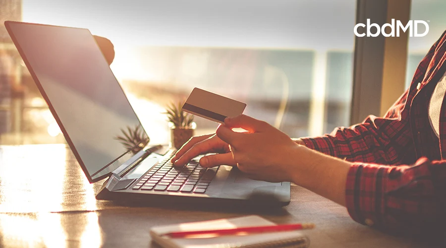 Person sitting down at a desk in front of a laptop they are using to shop with a card in one hand