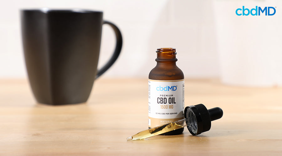 A coffee mug next to a bottle of cbdmd premium cbd oil 1500 mg natural sitting on a wooden table