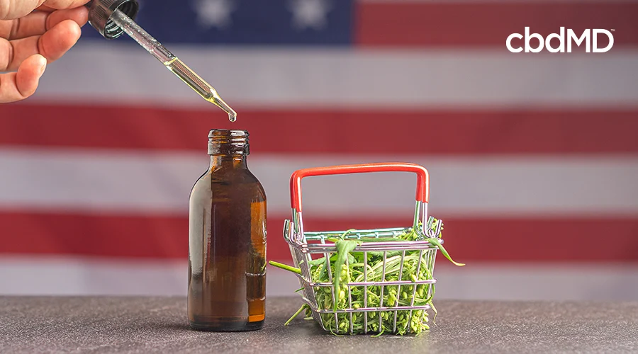 dropper going into tincture bottle with cannabis in shopping cart while usa flag is in the background