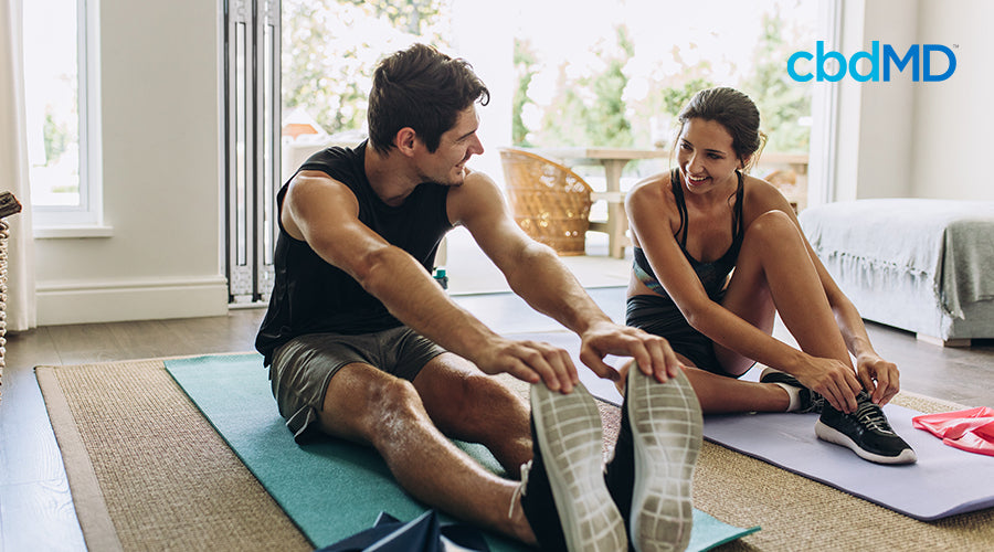 A man and a woman sitting down on exercise mats stretching