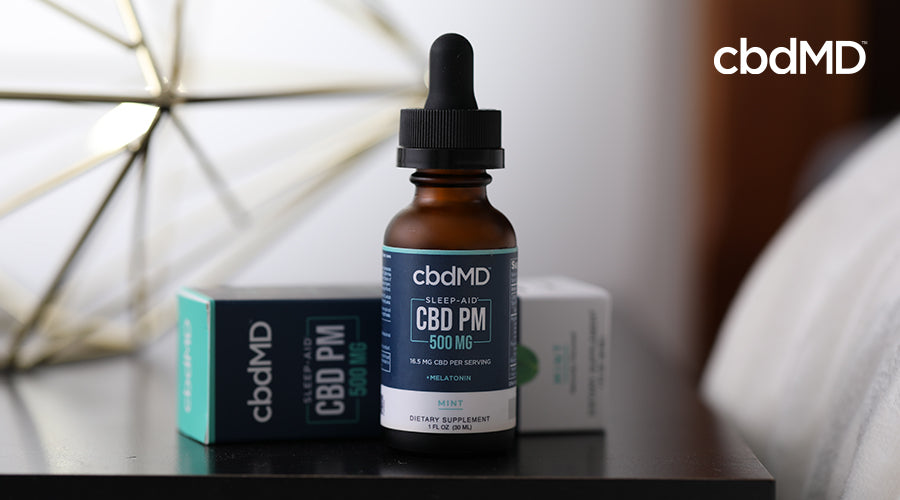 cbdMD sleep aid cbd pm 500 mg melatonin mint container with its box behind it on a nightstand next to a bed