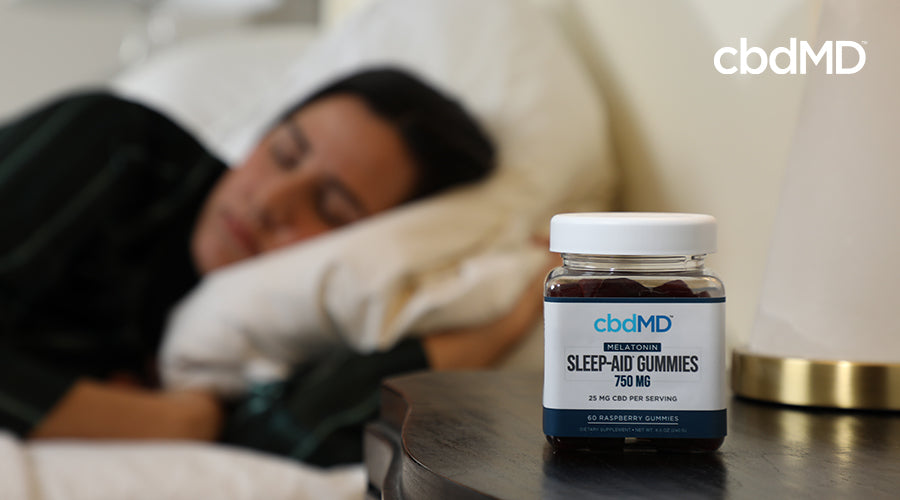 A woman sleeping next to a nightstand with cbdMD sleep aid gummies 750 mg raspberry container on it