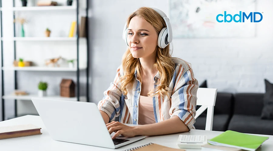 Woman sitting down at a desk using her laptop to study with headphones on her head