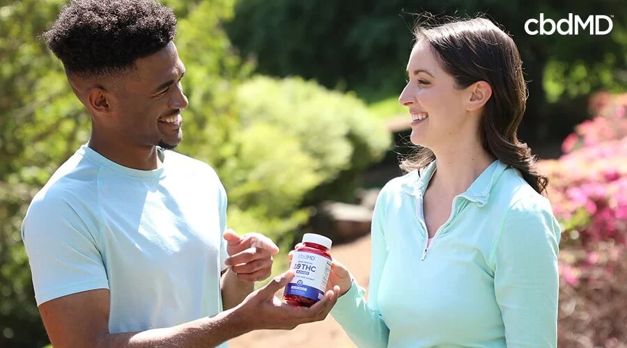 A man handing a woman a bottle of hemp derived delta 9 thc gummies blue razz 20 count while they are outside - cbdMD