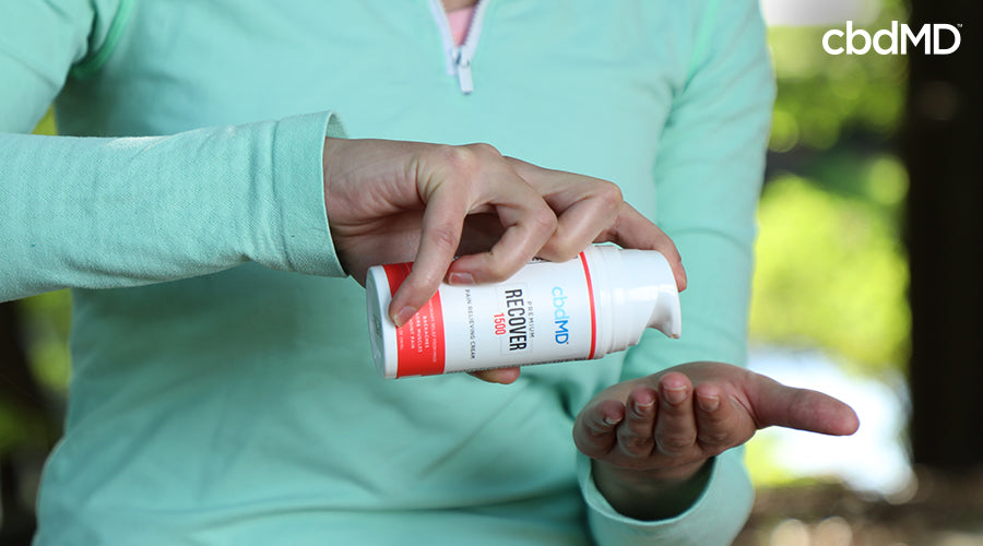 A woman holding recover cbd cream in her hand about to press cream out into her other hand - cbdMD