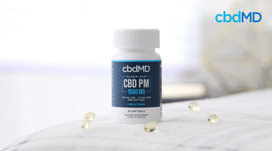 cbdMD sleep aid cbd pm 1500 mg melatonin bottle sitting on a bed with softgel capsules around it