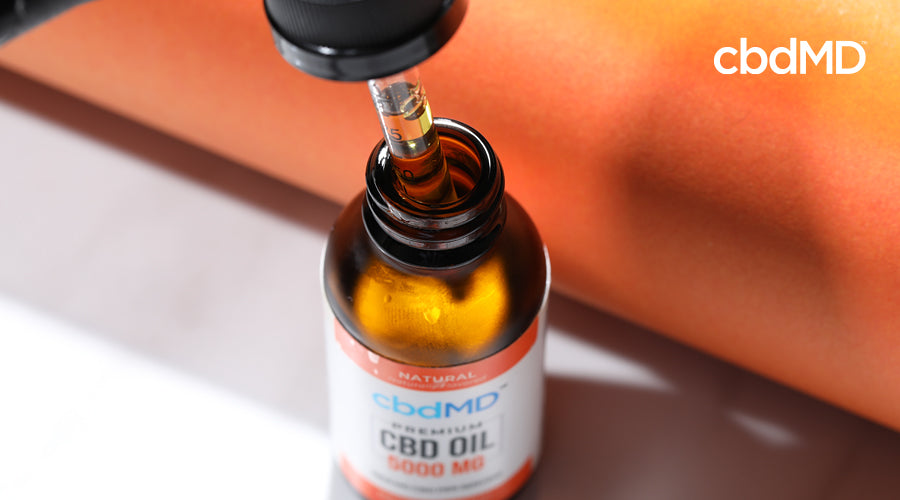 A bottle of cbd oil from cbdmd sits with the dropper slightly exposed and full