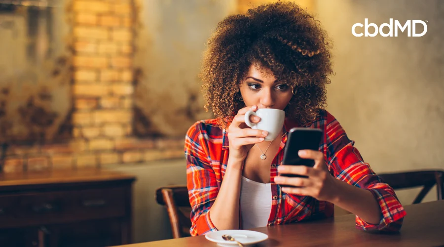 A beautiful woman in a flannel shirt looks at her phone while drinking coffee