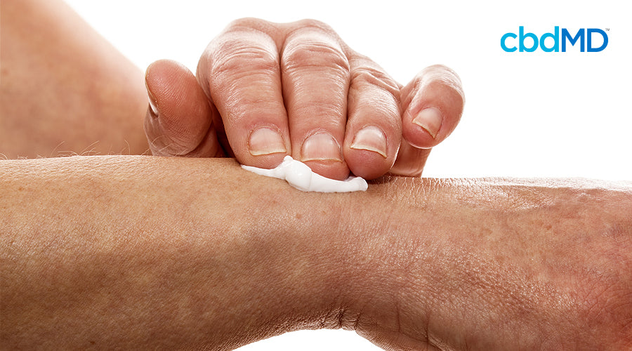 An arm rests up across the image with a hand rubbing white cbd cream at the wrist