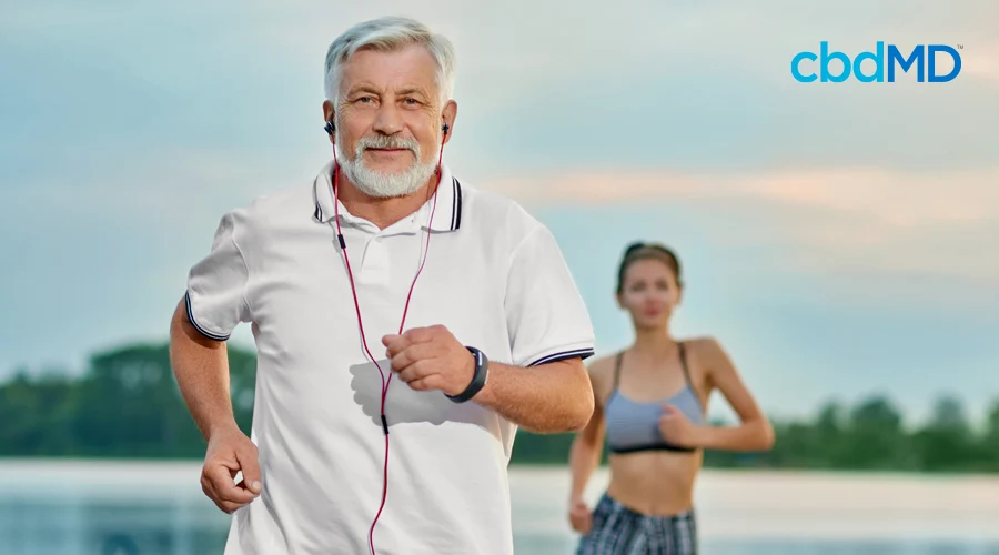 An older gentleman in a white polo shirt, jogs with headphones while an attractive woman follows him in the background