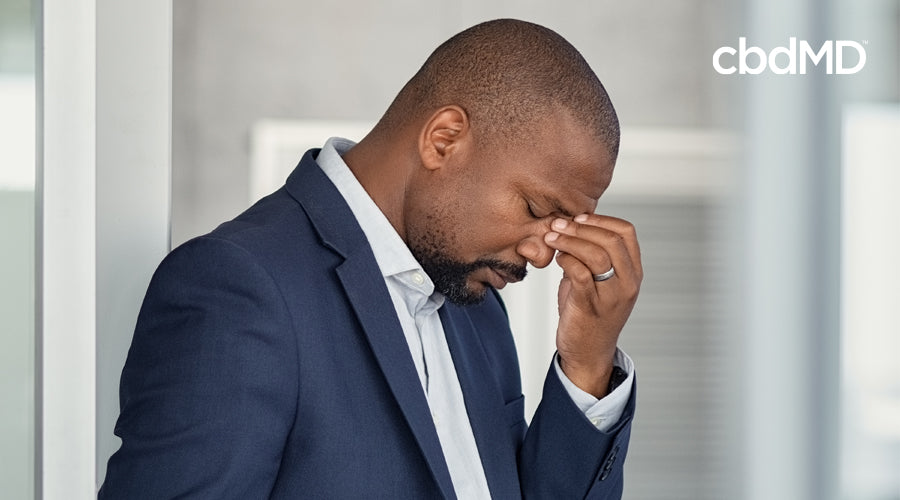 A business man holds his head at the bridge of his nose in apparent pain
