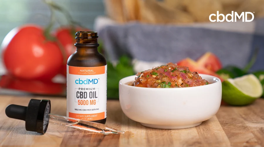 A bottle of 5000 mg CBD Oil from cbdMD sits beside a bowl of pico de gallo