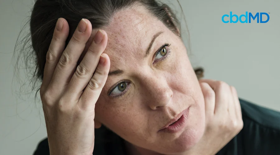 Dark-haired woman appears stressed with hands on forehead and rubbing neck