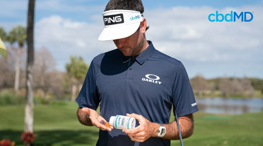 Bubba Watson stands on a golf course and gets ready to take two CBD gummies from cbdMD
