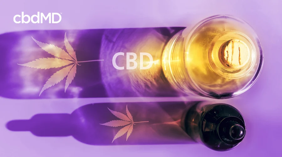 cbdMD's cbd oil in a clear glass corked bottle beside a brown glass dropper bottle