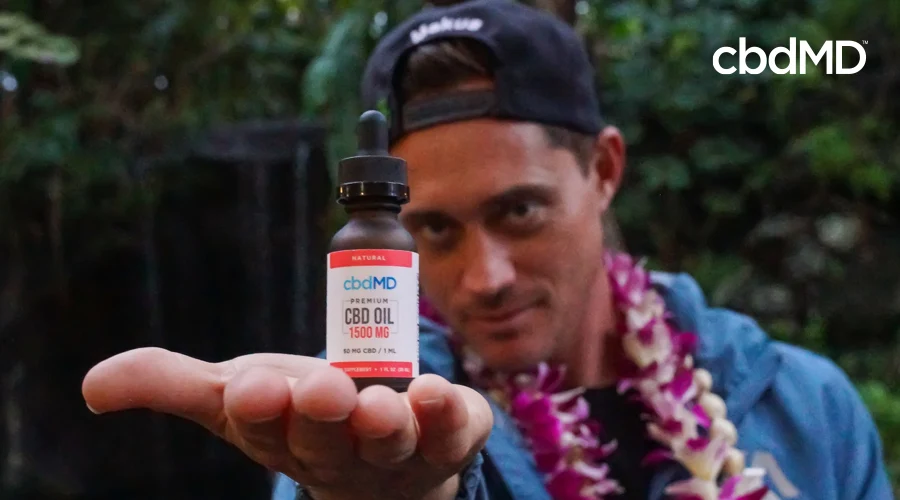 Surfer Makua Rothman stands with backwards hat holding 1500 mg Natural CBD oil from cbdMD in his palm