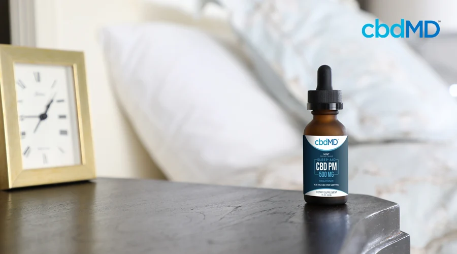 cbdMD sleep aid cbd pm 500 mg bottle sitting on a nightstand next to a bed and clock