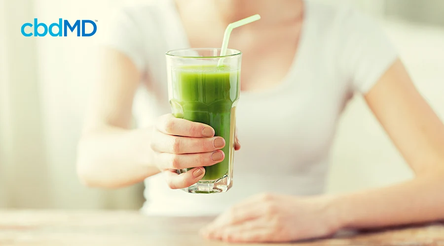 A woman in a white t-shirt reaches out to hand over a glass filled with green juice