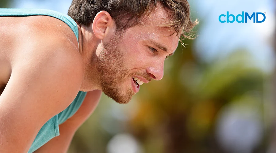A young, bearded man with sweat on his brow catches his breath after a workout