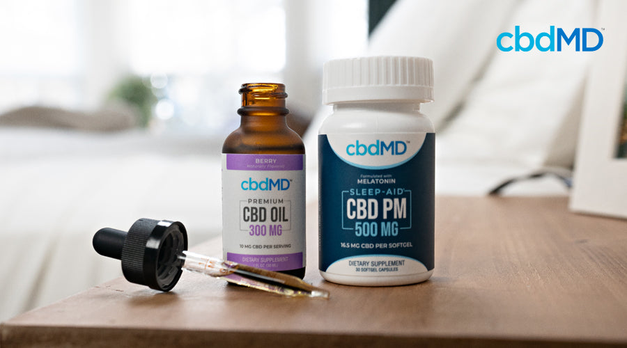 A bottle of 300 mg cbd oil and 500 mg cbd pm capsules from cbdmd sit on a nightstand