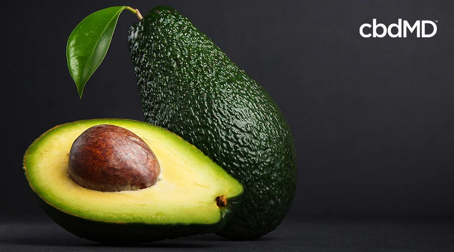 A whole avocado and a halved avocado sit next to each other against a black background