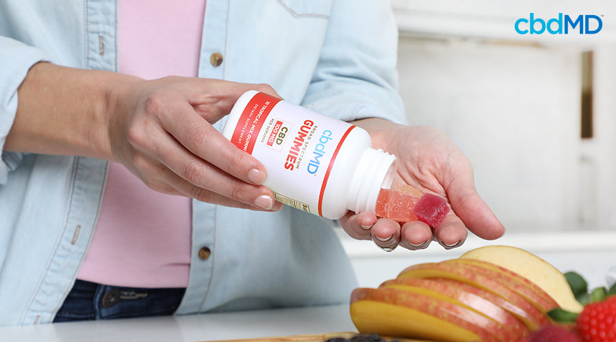 A woman holding broad spectrum gummies tropical mix in one hand while pouring cbd gummies out in her other hand - cbdMD
