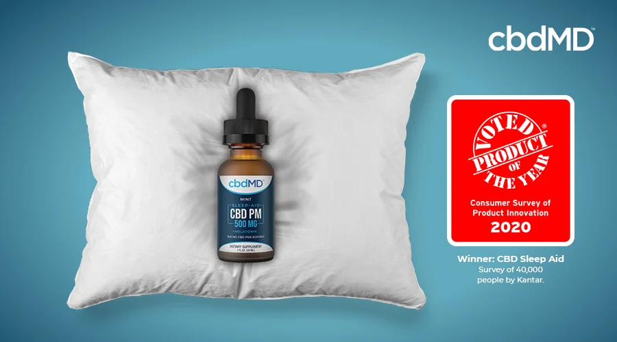 A bottle of 500 mg cbd pm tincture from cbdmd sits on a pillow next to the product of the year seal
