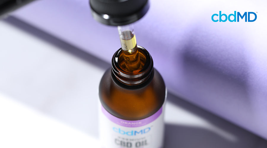 A bottle of cbd oil from cbdmd sits with a dropper partly out pulling a serving