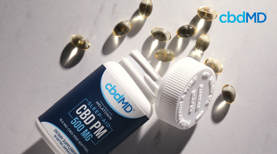 A bottle of cbd pm capsules lays on its side with capsules spilling out of the top