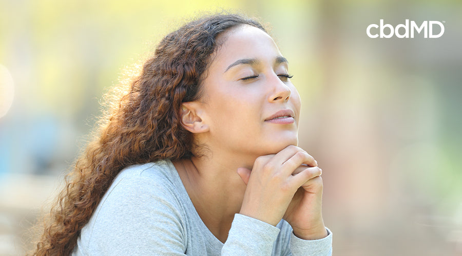 A olive skinned woman holds her hands beneath her chin as she closes her eyes