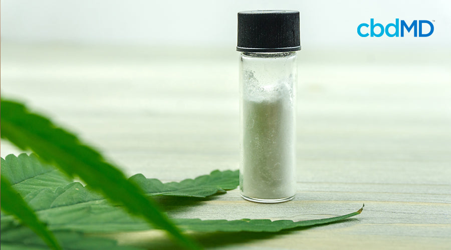 A vial of cbd isolate sits beside a hemp leaf
