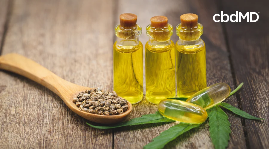 Three vials of hemp oil sit near a wooden spoon holding seeds and a hemp leaf