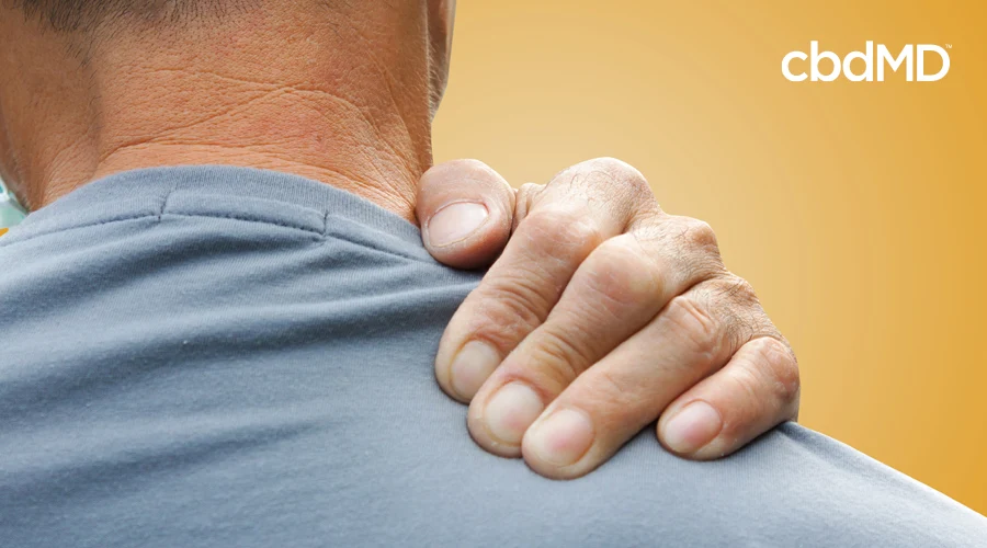 A man in a grey shirt rubes his shoulder in pain