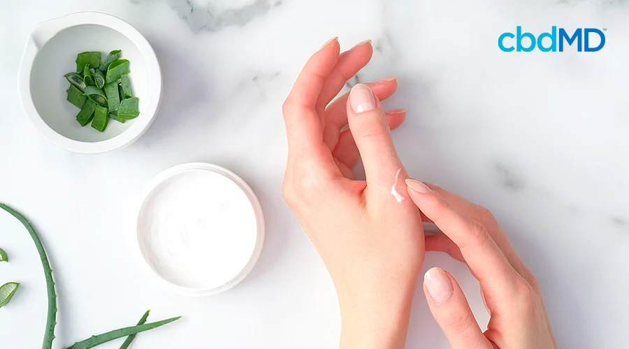 A woman rubs shea butter lotion on her hand over a marble table