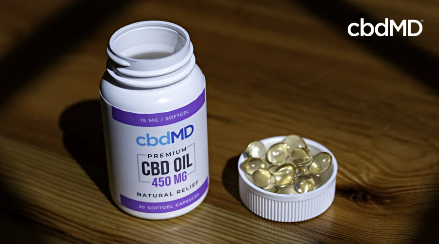 A bottle of 450 mg cbd softgel capsules from cbdmd sits on a nightstand the cap full of capsules
