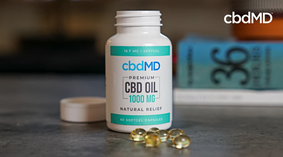 A bottle of 1000 mg cbd softgel capsules from cbdmd sits on a counter near some books