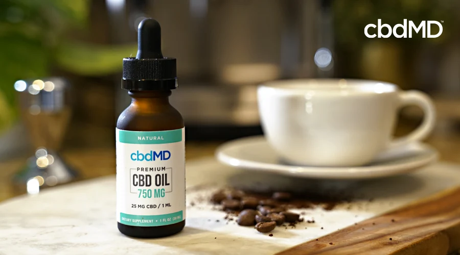 A bottle of 750 mg cbd oil tincture from cbdmd sits next to a cup of coffee
