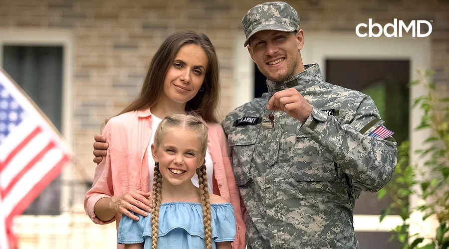 A military family stands together in front of their house with the american flag flying