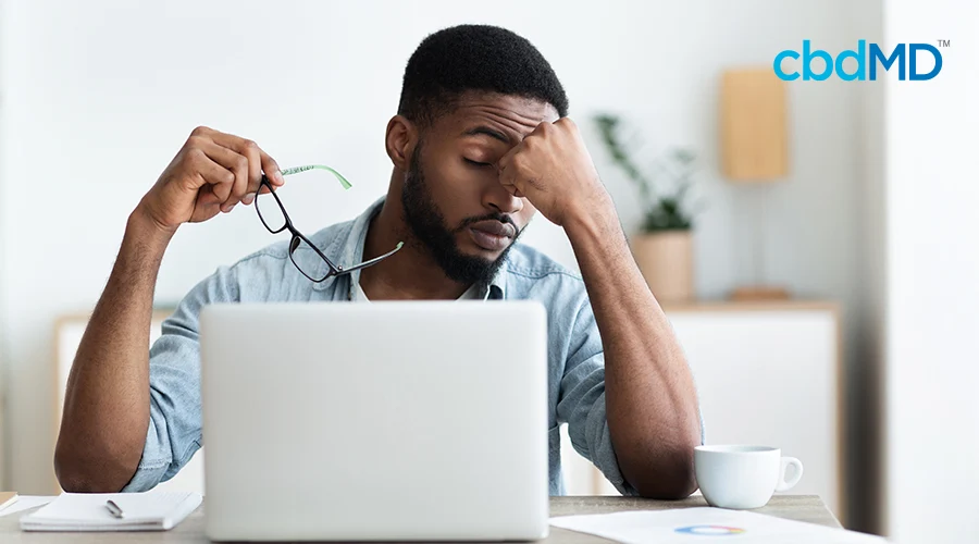 A man holds his glasses and rubs his nose as he sits in front of a computer
