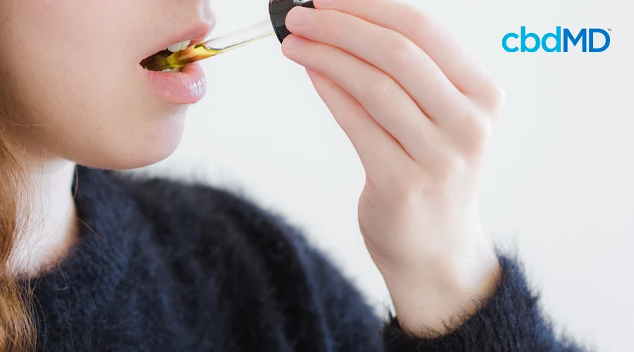 A woman in a fuzzy sweater holds up a dropper of CBD oil to take sublingually