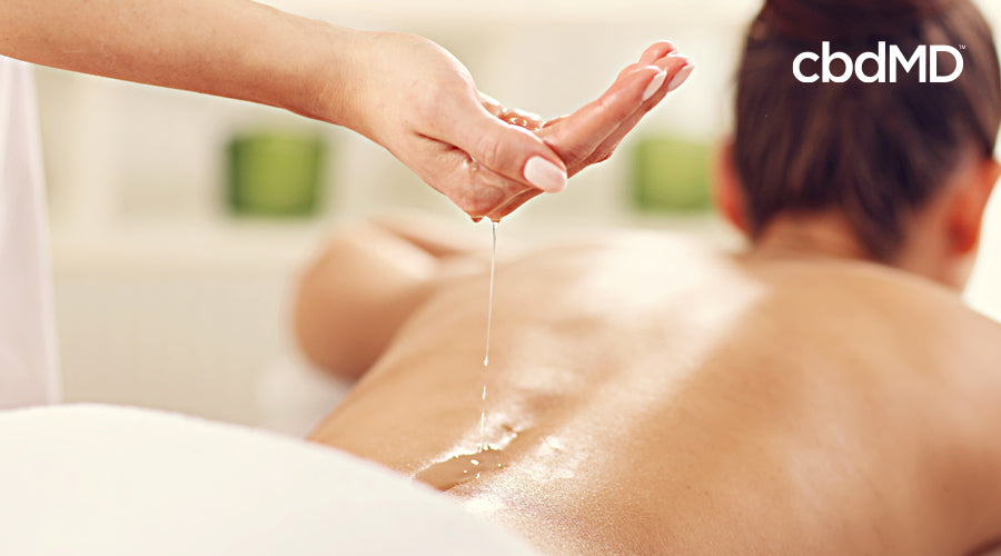 A woman lays on a table with cbd massage oil being applied to her bare back