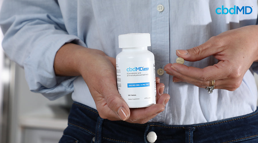 A woman holding max for pain 200 mg cbd 4 mg thc tablets in her hand and holding a tablet with her fingers - cbdMD