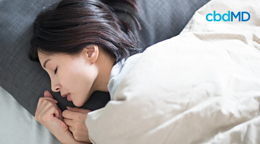 An attractive asian woman sleeps soundly under fluffy white blankets
