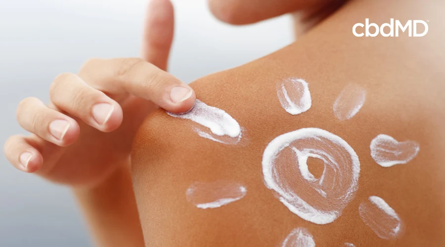 A woman draws a sun in sunscreen with her fingers on her bare shoulder