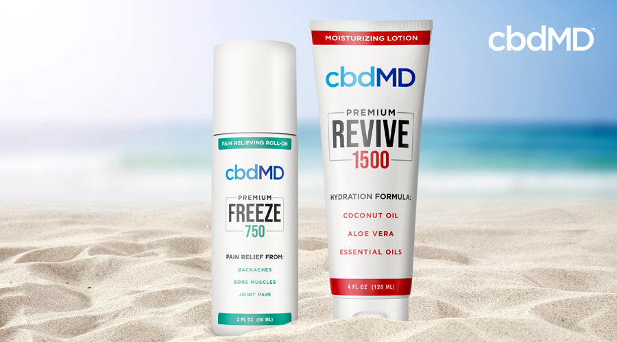 A bottle of 750 mg CBD Freeze and 1500 mg CBD Revive from cbdMD sit side by side on the sand