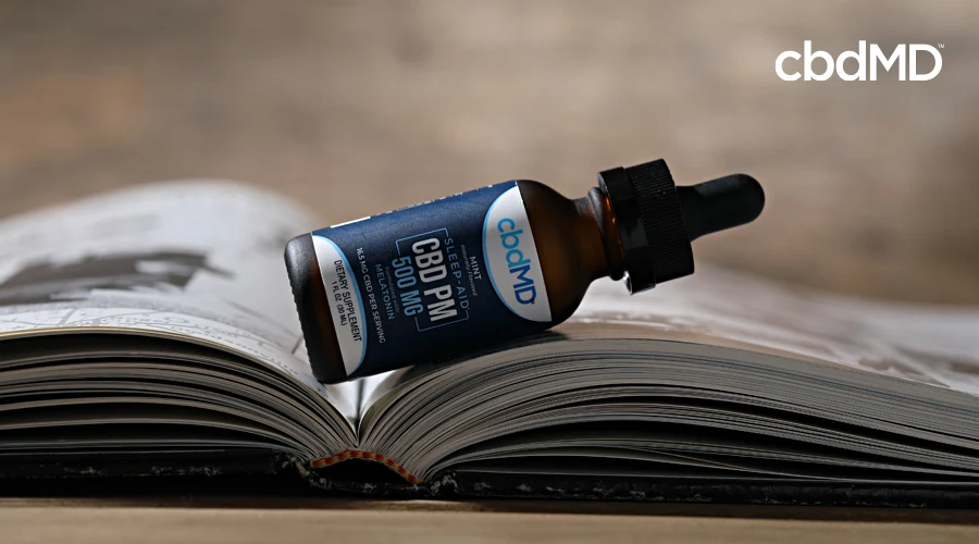 A bottle of cbd pm from cbdmd sits side ways on a book