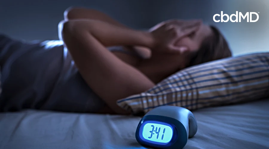 A woman rubs her face in frustration as she lies awake with an alarm clock on her side table