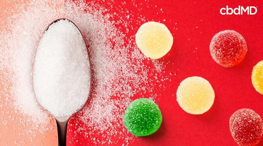 A spoon full of sugar spilling over next to a group of gummies